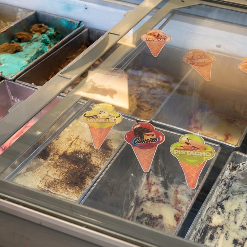 Glass-front gelato display case showing colorful flavors including vanilla, chocolate, pistachio, cookies and cream, and strawberry.