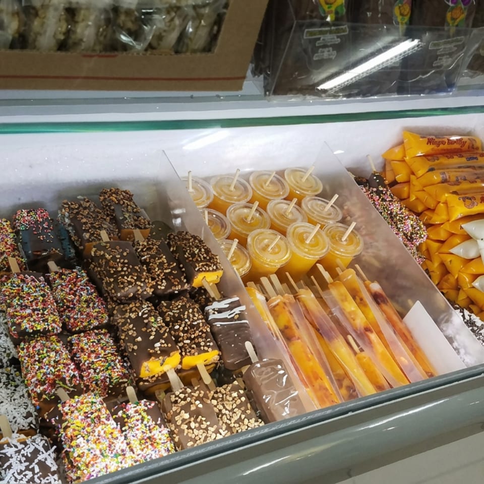 Freezer display filled with chocolate- and coconut-coated dessert bars, colorful sprinkles, fruit popsicles, and packaged treats.