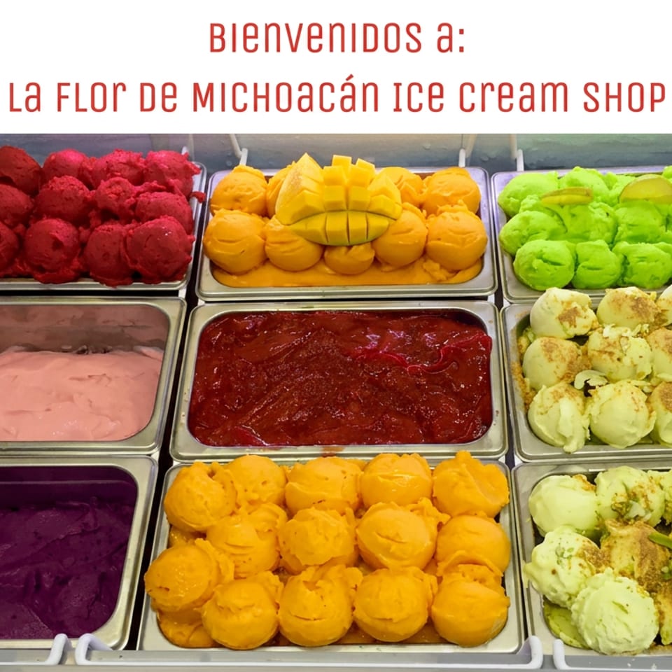 Colorful trays of Mexican ice cream flavors, including mango, lime, berry, and fruit-topped scoops, displayed beneath a welcome sign.
