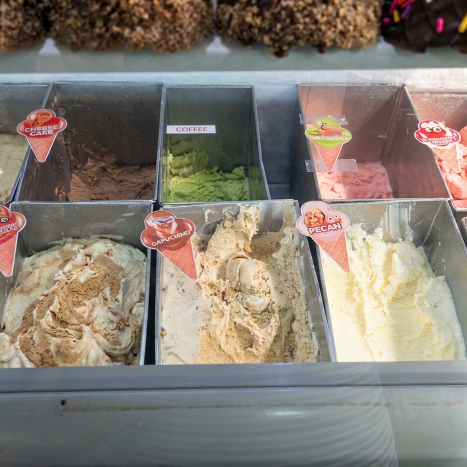 Open freezer display showcasing assorted ice cream flavors, including coffee, strawberry, pecan, cappuccino, and sprinkle-topped varieties.